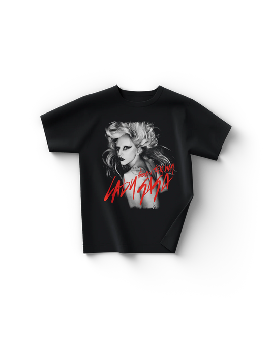 Black Lady Gaga t-shirt with a grayscale portrait of Gaga wearing bold black eyeliner and voluminous blonde hair, overlaid with red handwritten text reading “Born This Way” and “Lady Gaga.” The striking design captures Gaga’s signature theatrical style from the Born This Way era.

